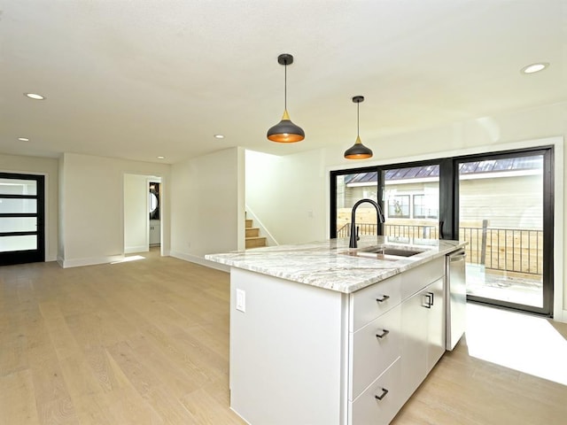 kitchen with light wood finished floors, a sink, light stone counters, and stainless steel dishwasher