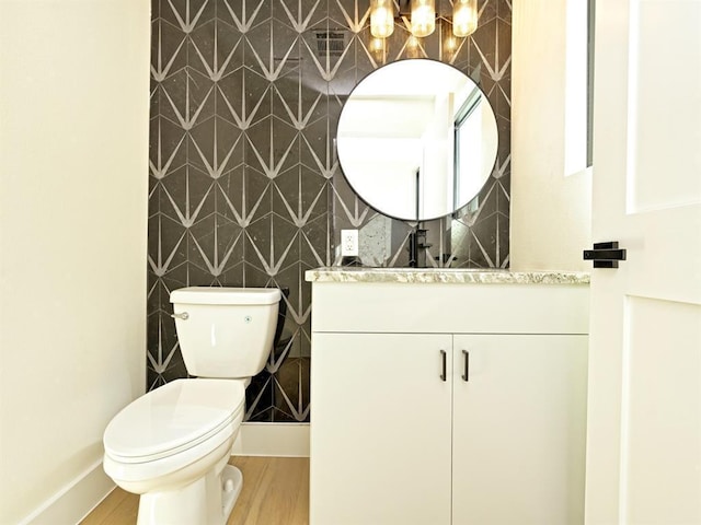 half bath featuring toilet, vanity, baseboards, and wood finished floors