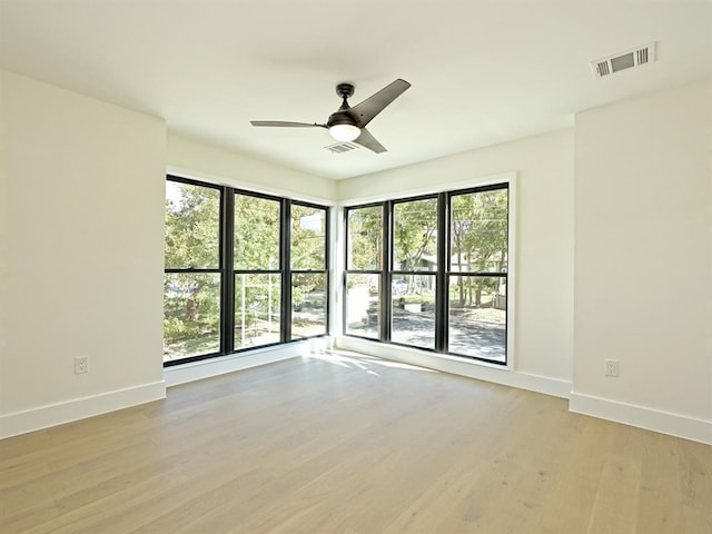 spare room featuring light wood-style flooring, a ceiling fan, visible vents, and baseboards