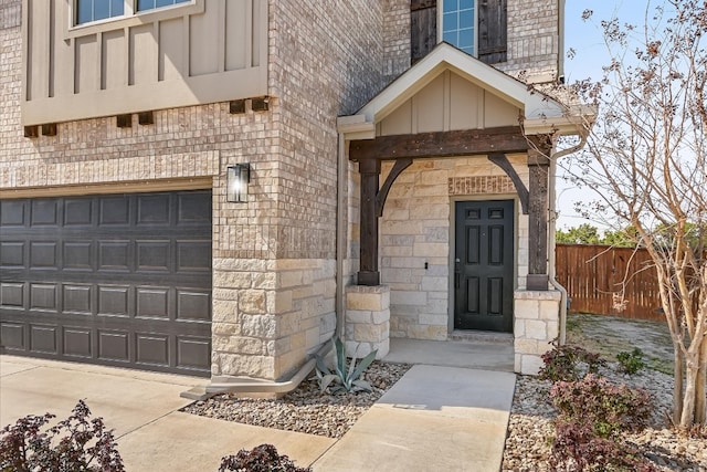 entrance to property featuring an attached garage, fence, board and batten siding, and stone siding