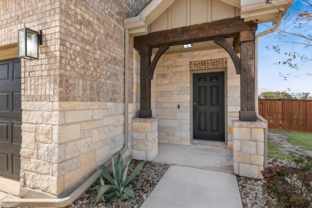 doorway to property featuring stone siding, board and batten siding, a garage, and fence