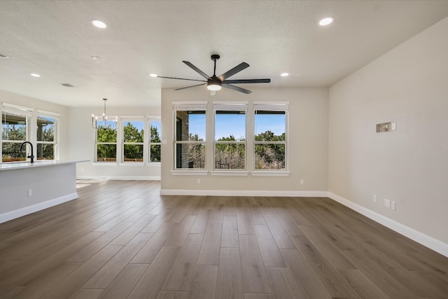 unfurnished living room with recessed lighting, ceiling fan with notable chandelier, dark wood-type flooring, and baseboards