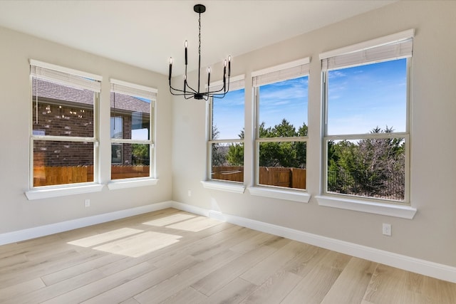 unfurnished dining area featuring a chandelier, baseboards, and wood finished floors