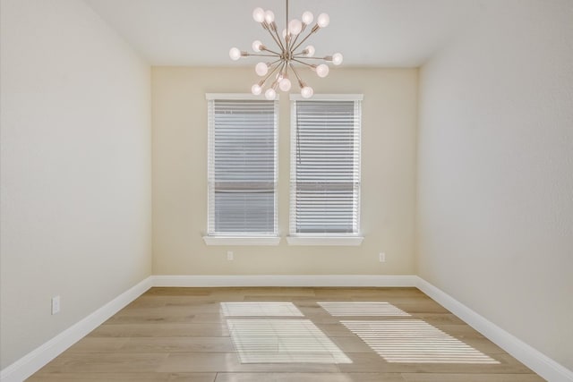 empty room with baseboards, an inviting chandelier, and wood finished floors