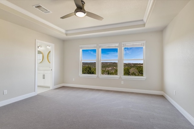 carpeted spare room featuring a tray ceiling, visible vents, baseboards, and a ceiling fan