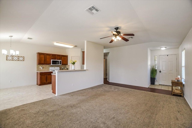 unfurnished living room featuring visible vents, lofted ceiling, light colored carpet, and ceiling fan with notable chandelier