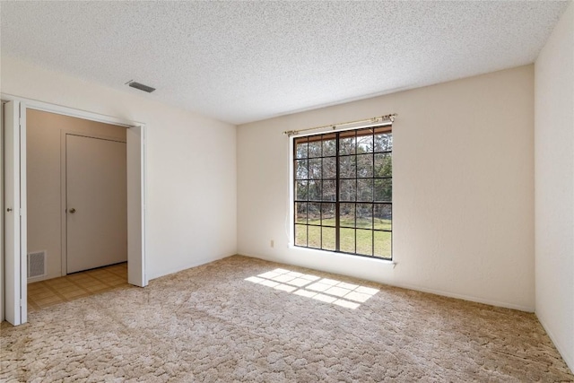 carpeted spare room with visible vents and a textured ceiling