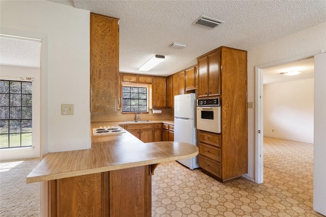 kitchen with white appliances, brown cabinetry, visible vents, a peninsula, and a sink