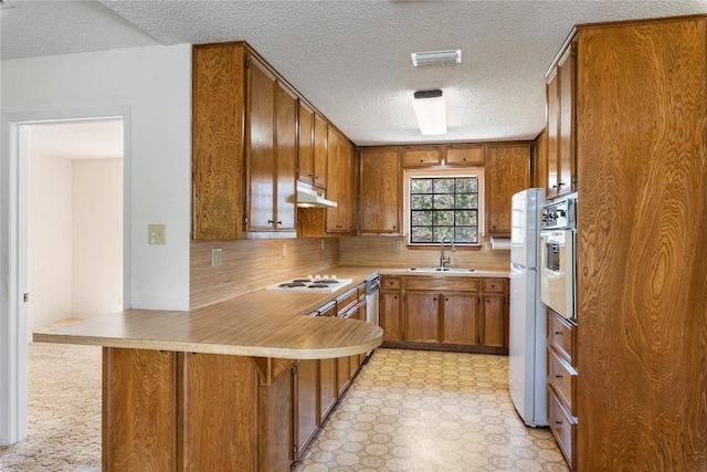 kitchen with brown cabinets, a sink, under cabinet range hood, white appliances, and light floors