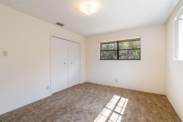 unfurnished bedroom featuring visible vents, a textured ceiling, a closet, and carpet flooring