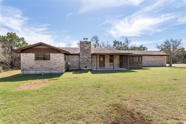 back of property featuring a patio area, a lawn, brick siding, and a chimney