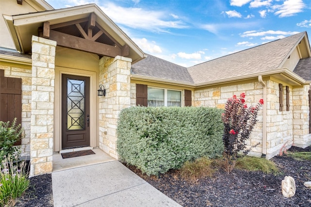 doorway to property with stone siding and a shingled roof