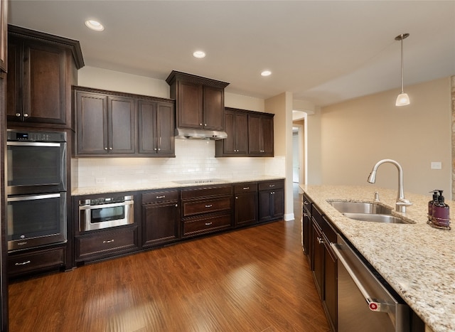 kitchen featuring backsplash, dark wood-type flooring, under cabinet range hood, stainless steel appliances, and a sink