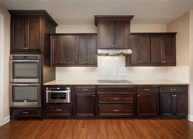 kitchen featuring under cabinet range hood, dark wood finished floors, double oven, light stone counters, and black electric cooktop