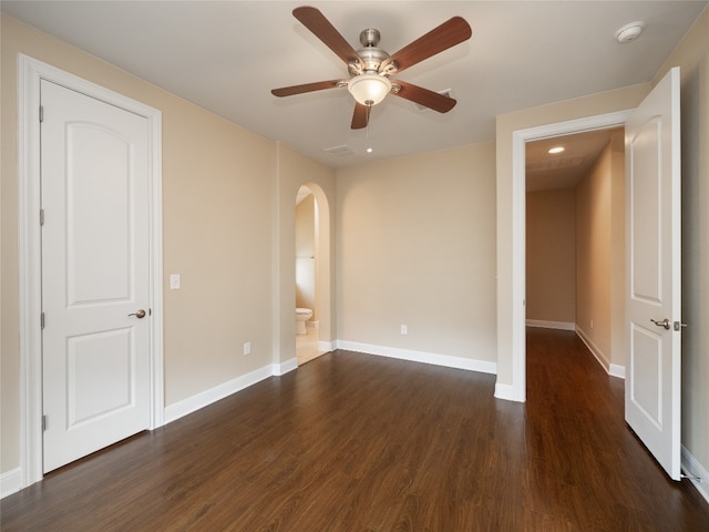 spare room featuring ceiling fan, baseboards, arched walkways, and dark wood-style floors