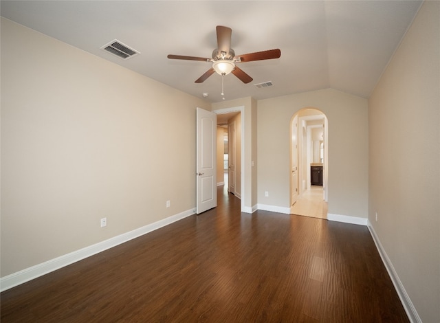 empty room with dark wood-style floors, baseboards, visible vents, arched walkways, and ceiling fan