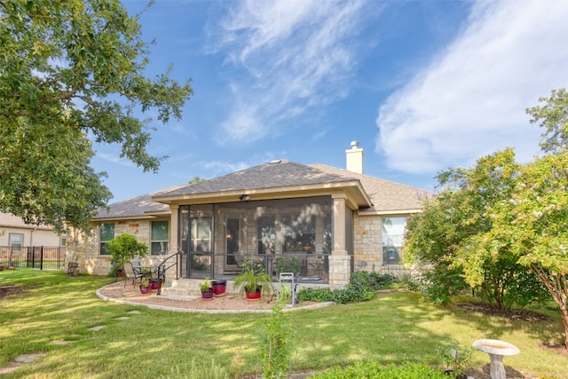 rear view of house with a lawn, stone siding, a sunroom, fence, and a shingled roof