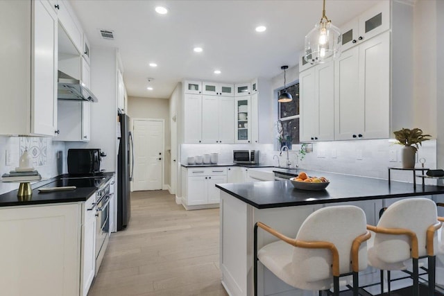 kitchen featuring visible vents, a kitchen bar, a peninsula, stainless steel appliances, and white cabinetry