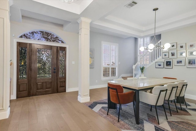 dining area with wood finished floors, visible vents, a tray ceiling, decorative columns, and a chandelier