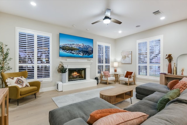 living area with a glass covered fireplace, recessed lighting, wood finished floors, and ceiling fan