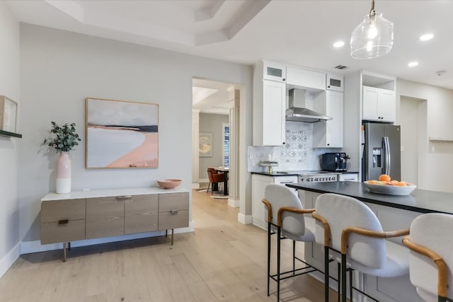 kitchen featuring light wood-style floors, appliances with stainless steel finishes, a kitchen breakfast bar, wall chimney exhaust hood, and backsplash