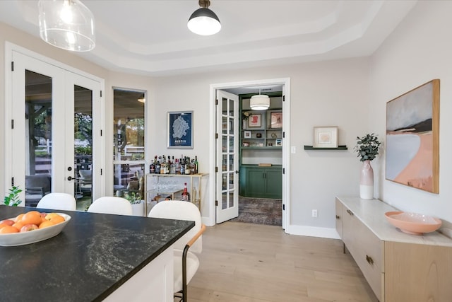 interior space with a tray ceiling, french doors, hanging light fixtures, and light wood finished floors