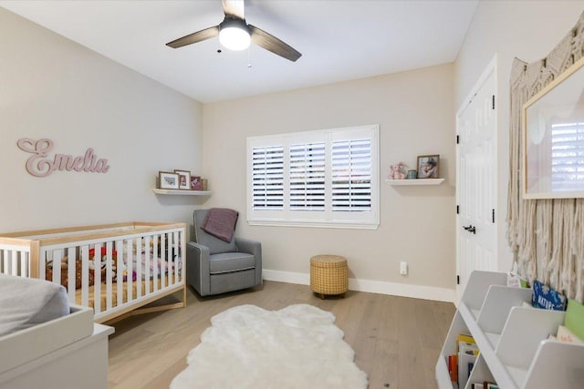 bedroom featuring ceiling fan, a crib, baseboards, and wood finished floors