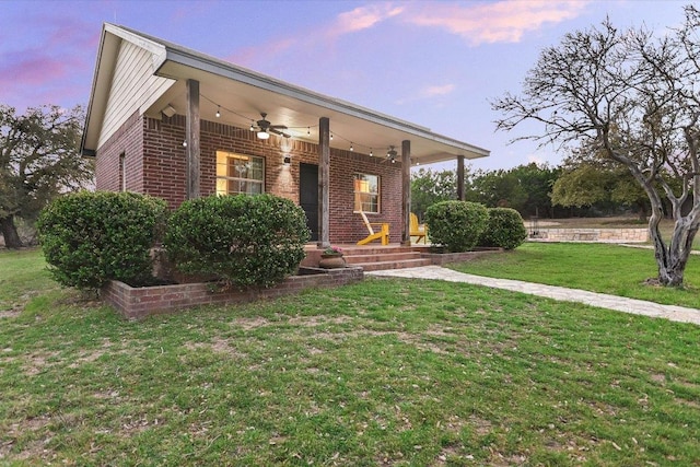 view of front of property featuring brick siding, a lawn, a porch, and a ceiling fan