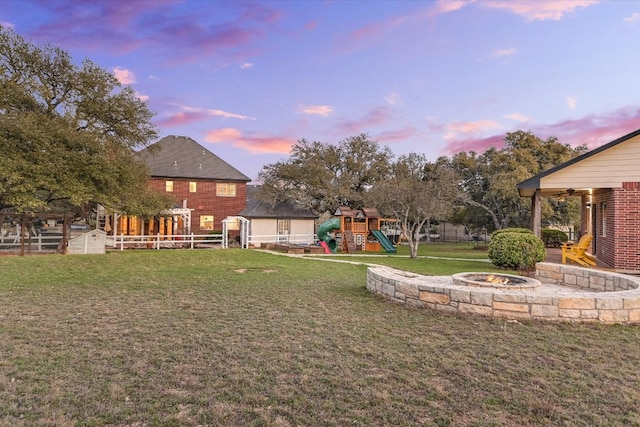 yard at dusk featuring a patio, a playground, fence, and an outdoor fire pit