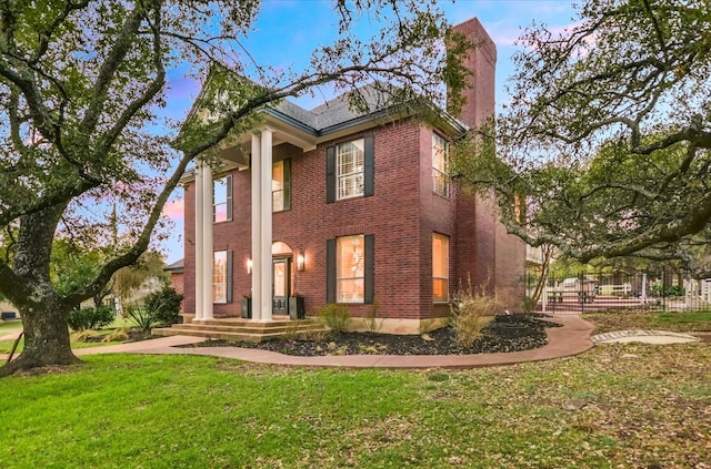 greek revival house with brick siding, a chimney, and a front yard