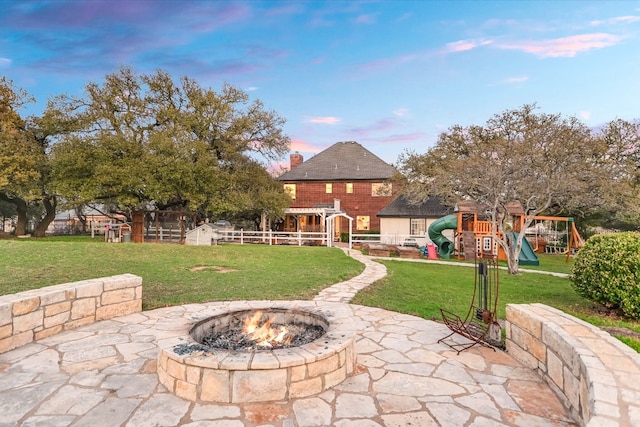 view of patio with a playground, fence, and an outdoor fire pit