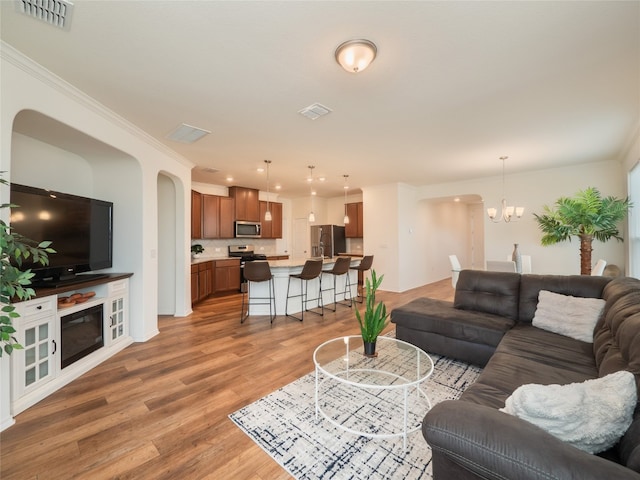 living room featuring visible vents, a notable chandelier, ornamental molding, and light wood finished floors