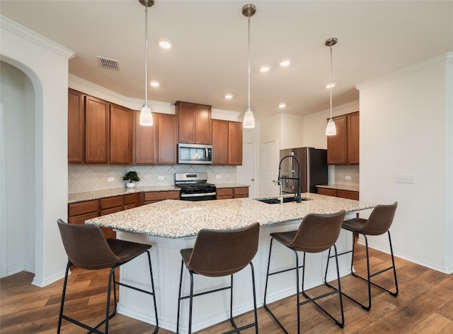 201 Teller Dr, Lockhart, TX 78644 - kitchen featuring appliances with stainless steel finishes, a sink, a kitchen island with sink, brown cabinets, and tasteful backsplash