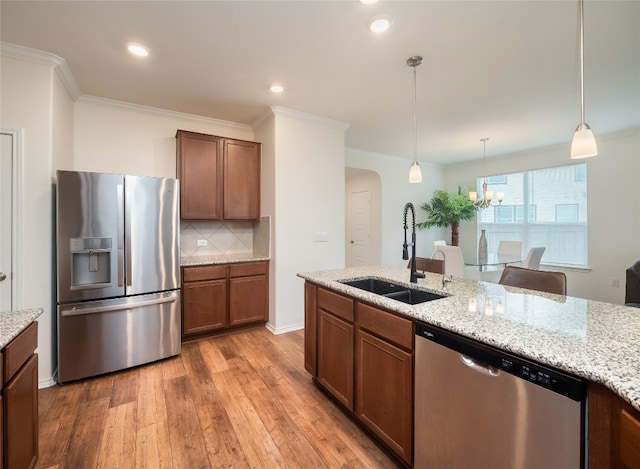 kitchen with arched walkways, a sink, stainless steel appliances, decorative light fixtures, and light wood-type flooring