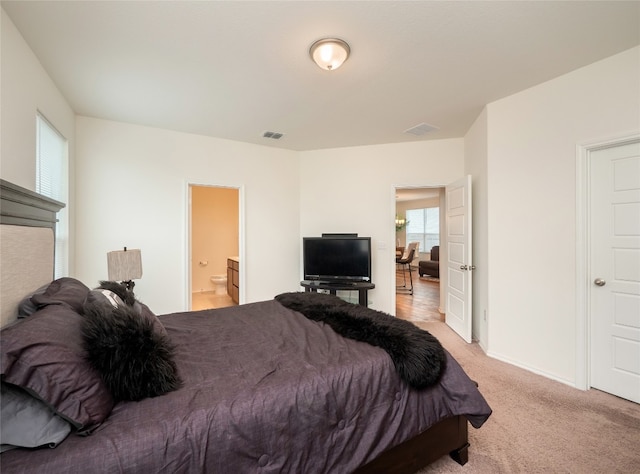 bedroom featuring visible vents, light colored carpet, and connected bathroom