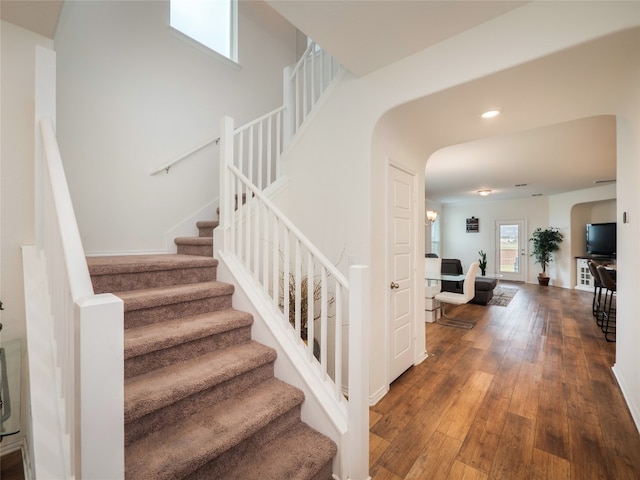 stairway with hardwood / wood-style floors, recessed lighting, and arched walkways