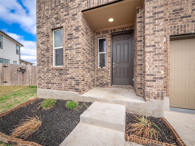 view of exterior entry featuring fence and brick siding