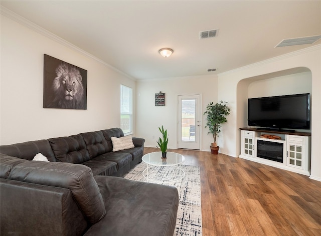 living room with arched walkways, visible vents, crown molding, and wood finished floors