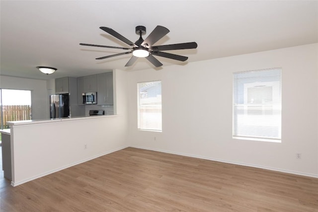 unfurnished living room with plenty of natural light, a ceiling fan, light wood-type flooring, and baseboards