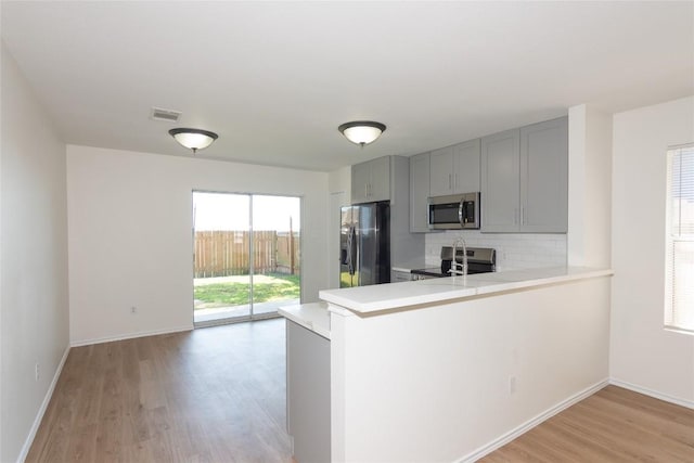 kitchen with visible vents, gray cabinetry, backsplash, stainless steel appliances, and light countertops