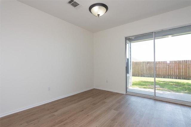 spare room featuring light wood finished floors, visible vents, and baseboards