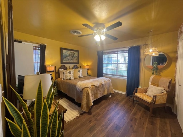 bedroom with a ceiling fan, multiple windows, visible vents, and dark wood-style flooring