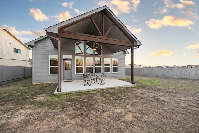 back of property at dusk with a ceiling fan, a patio area, a fenced backyard, and a lawn