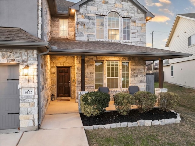 doorway to property with covered porch, stone siding, and a shingled roof