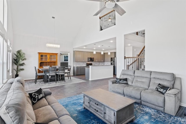 living room with dark wood-type flooring, stairway, ceiling fan with notable chandelier, and baseboards