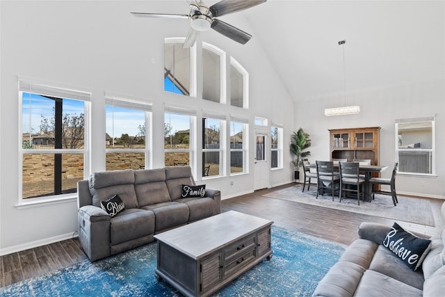 living room featuring baseboards, high vaulted ceiling, wood finished floors, and ceiling fan with notable chandelier