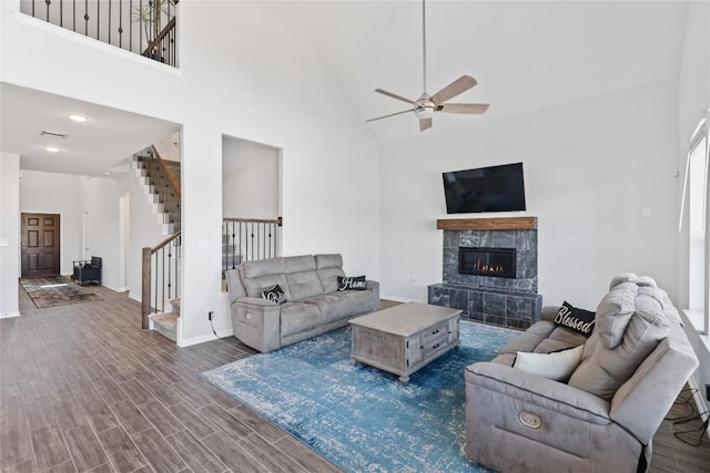 living area featuring high vaulted ceiling, dark wood-style flooring, a fireplace, ceiling fan, and stairs