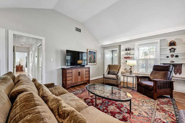 living room with wood finished floors, visible vents, baseboards, attic access, and lofted ceiling