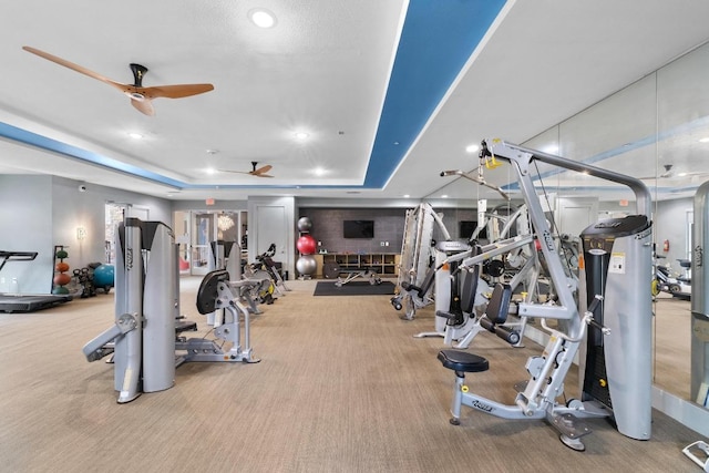 gym with a tray ceiling, carpet flooring, and ceiling fan