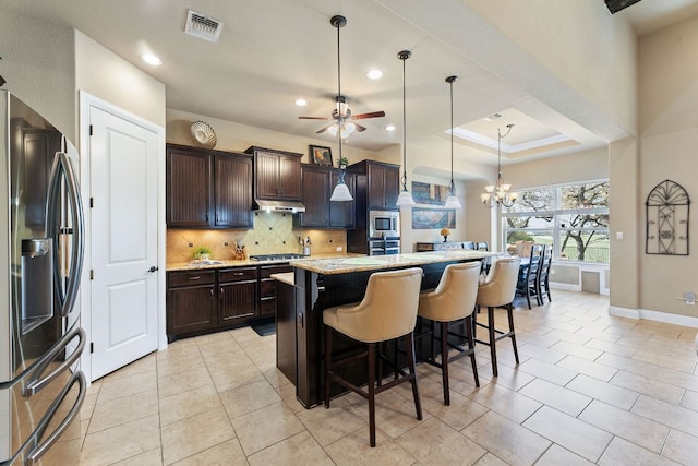 kitchen featuring dark brown cabinets, backsplash, under cabinet range hood, ceiling fan with notable chandelier, and appliances with stainless steel finishes